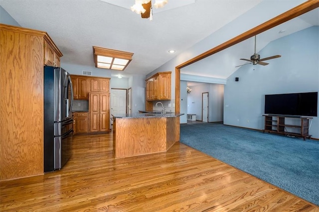 kitchen featuring brown cabinetry, dark countertops, open floor plan, freestanding refrigerator, and a peninsula