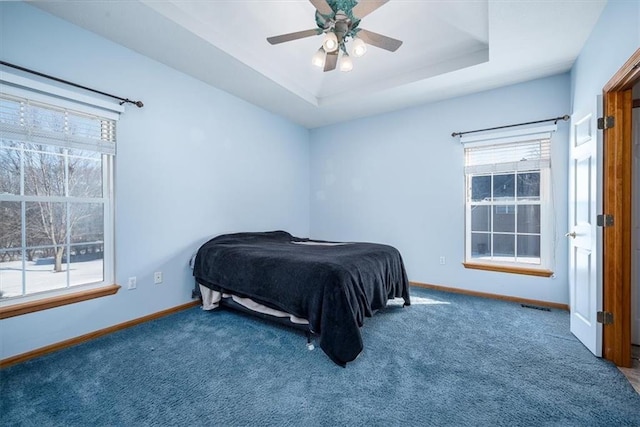 bedroom with a tray ceiling, multiple windows, visible vents, and baseboards