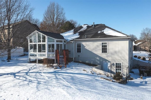 snow covered rear of property with stairway and a sunroom