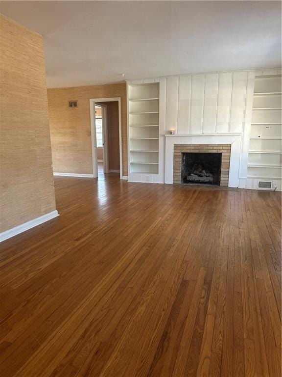 unfurnished living room with baseboards, visible vents, dark wood finished floors, built in features, and a fireplace