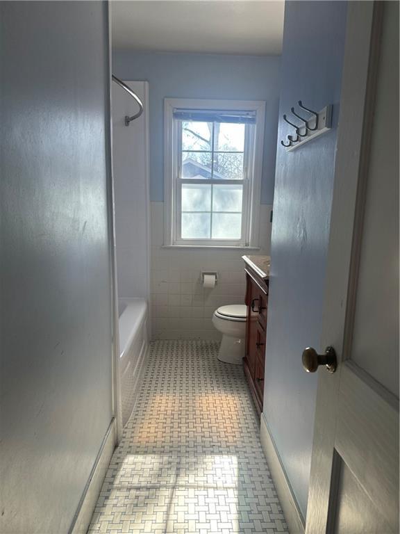 bathroom with tile walls, wainscoting, vanity, and toilet