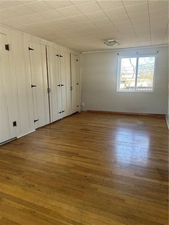 unfurnished bedroom with two closets, baseboards, and wood finished floors