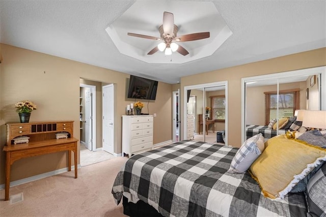 bedroom featuring a textured ceiling, ceiling fan, light carpet, multiple closets, and a raised ceiling