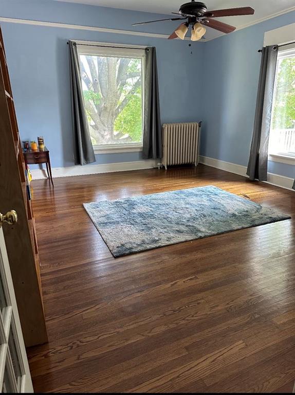 interior space with baseboards, radiator heating unit, ceiling fan, wood finished floors, and crown molding