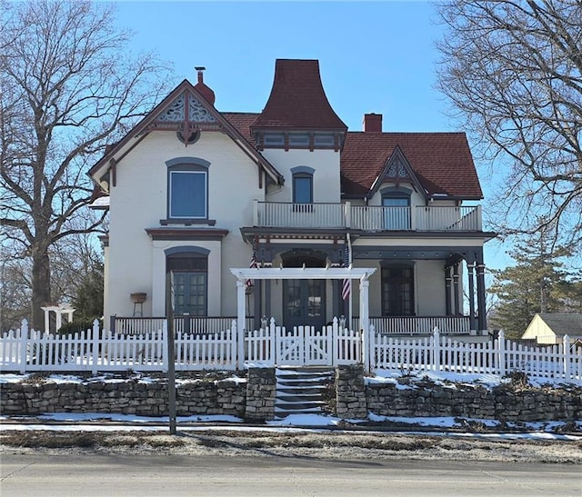 victorian home with a balcony, a fenced front yard, and a chimney