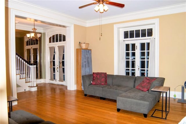 living area featuring wood finished floors, stairs, crown molding, french doors, and ceiling fan with notable chandelier