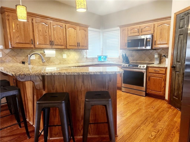 kitchen with a breakfast bar, light wood finished floors, a peninsula, and stainless steel appliances