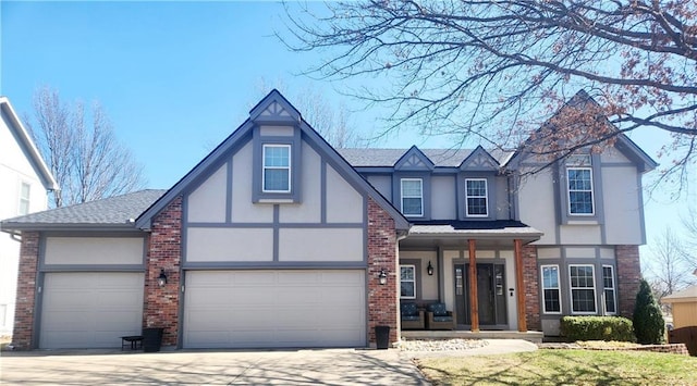 tudor house with stucco siding, driveway, a shingled roof, a garage, and brick siding