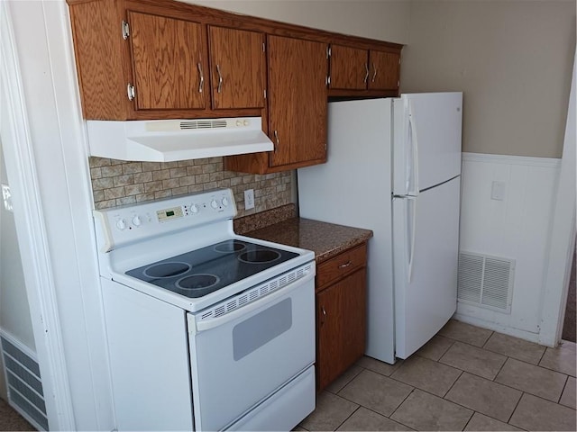 kitchen with under cabinet range hood, white appliances, visible vents, brown cabinets, and dark countertops