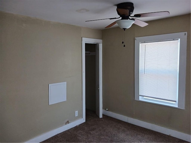 empty room featuring a ceiling fan, dark colored carpet, and baseboards