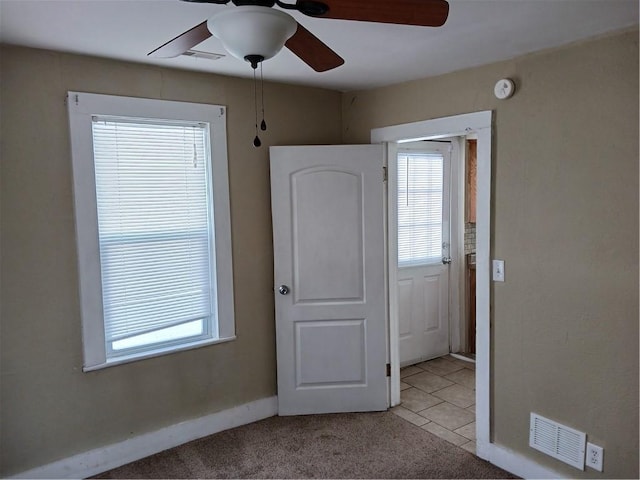 empty room with light tile patterned floors, plenty of natural light, visible vents, and light colored carpet