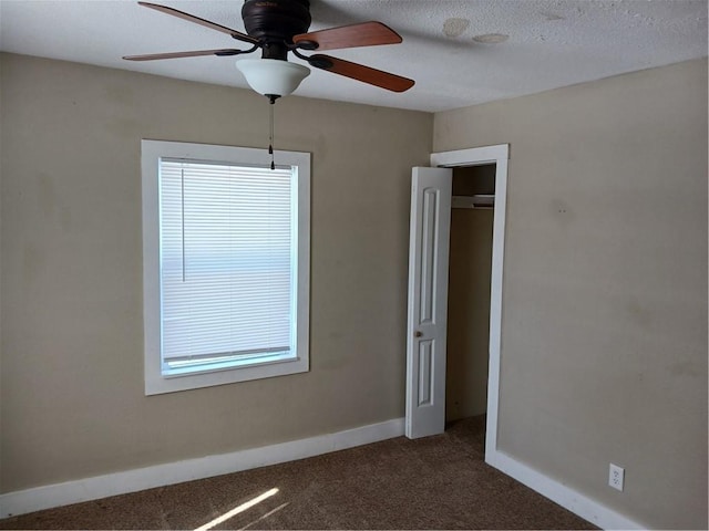 unfurnished room with a ceiling fan, dark colored carpet, a textured ceiling, and baseboards