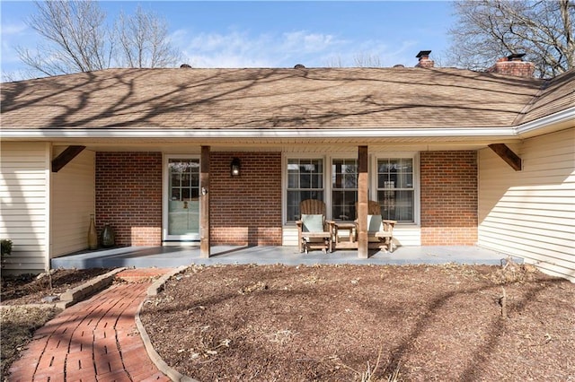 back of property with roof with shingles, a chimney, a porch, and brick siding