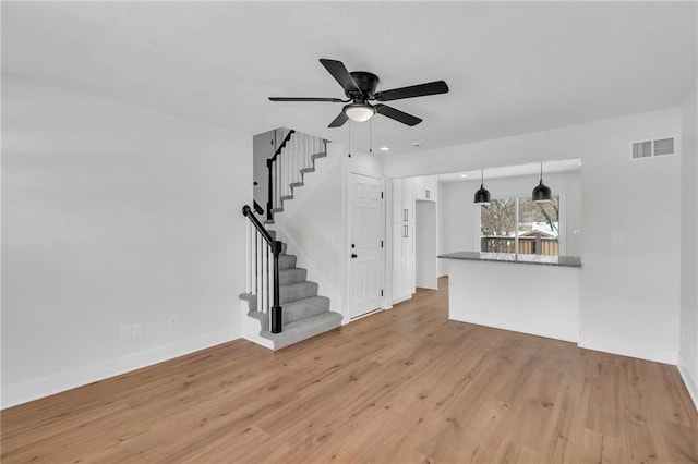 unfurnished living room with stairs, baseboards, visible vents, and light wood-style floors