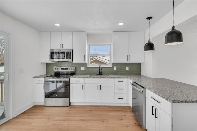 kitchen with decorative backsplash, a peninsula, stainless steel appliances, light wood-style floors, and a sink