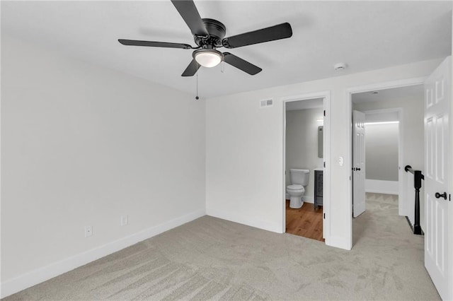 unfurnished bedroom with carpet floors, a ceiling fan, visible vents, baseboards, and ensuite bath