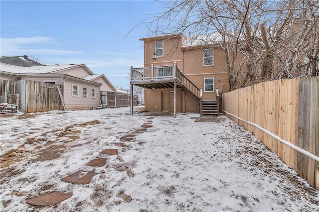 snow covered house with a fenced backyard, stairs, a deck, and stucco siding