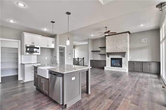 kitchen with stainless steel appliances, a sink, white cabinets, open floor plan, and decorative light fixtures