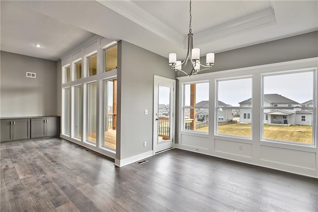 unfurnished dining area with dark wood-style floors, visible vents, a tray ceiling, and a notable chandelier