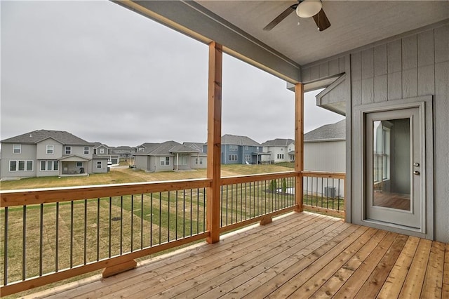 wooden deck featuring ceiling fan, a lawn, and a residential view