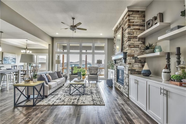 living room with ceiling fan with notable chandelier, dark wood-style flooring, and a fireplace