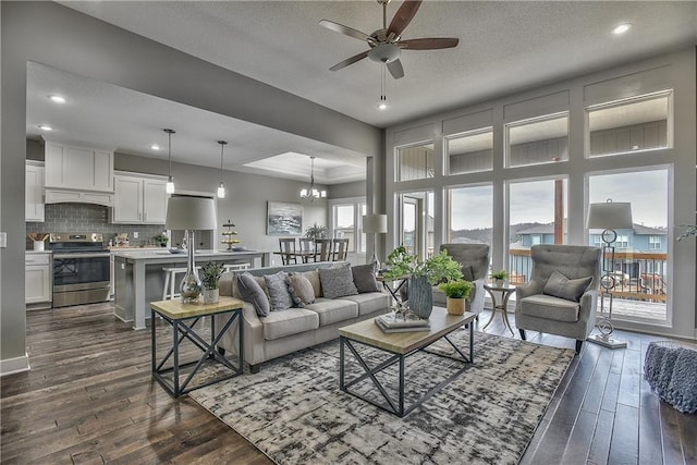 living room featuring a textured ceiling, recessed lighting, ceiling fan with notable chandelier, dark wood-type flooring, and a tray ceiling