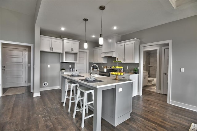 kitchen with pendant lighting, electric stove, a center island with sink, light countertops, and white cabinets