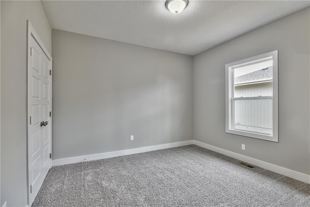 carpeted spare room featuring a textured ceiling, visible vents, and baseboards