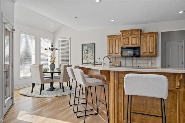 kitchen featuring brown cabinets, light countertops, decorative backsplash, light wood-style floors, and black microwave