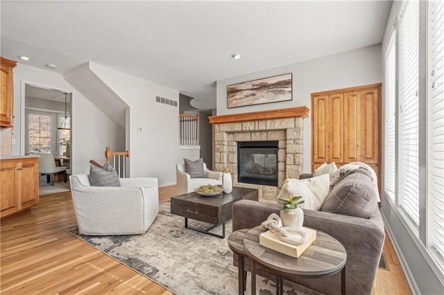 living area featuring visible vents, baseboards, light wood-style flooring, a stone fireplace, and recessed lighting