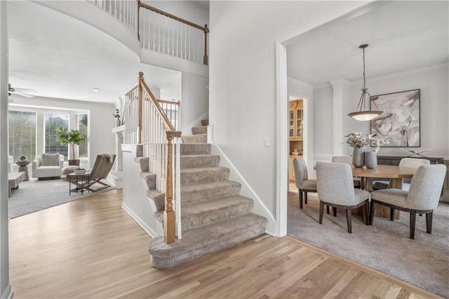 stairway with baseboards, a ceiling fan, a towering ceiling, wood finished floors, and crown molding