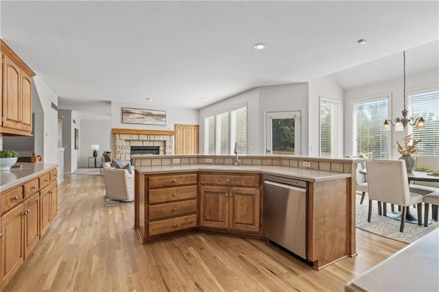 kitchen with a stone fireplace, a sink, open floor plan, hanging light fixtures, and dishwasher