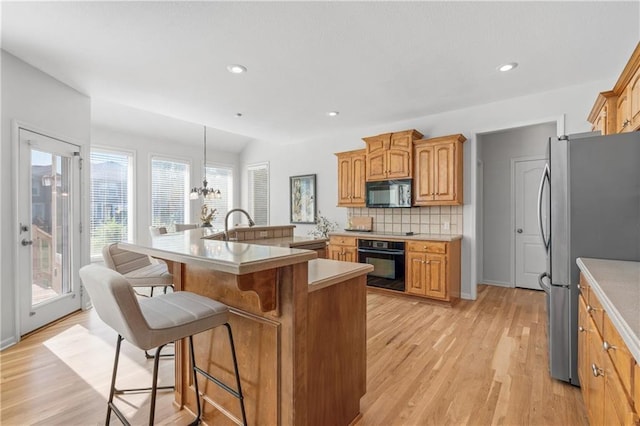 kitchen with a breakfast bar area, hanging light fixtures, light countertops, black appliances, and a center island with sink