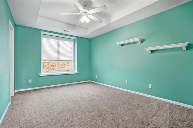 unfurnished room featuring visible vents, baseboards, a ceiling fan, a raised ceiling, and carpet flooring