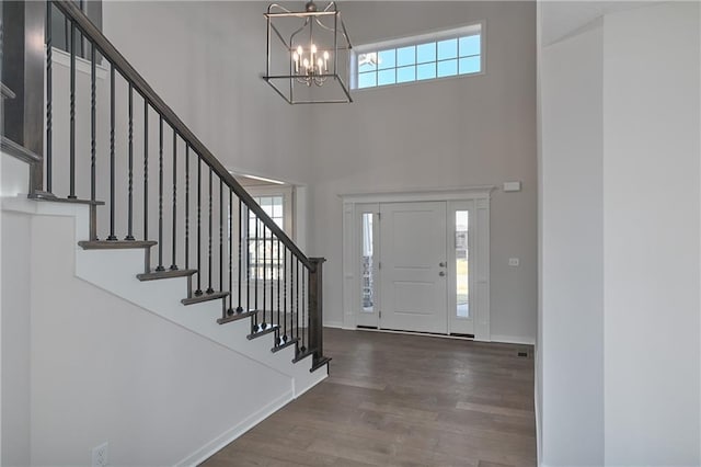 foyer entrance featuring wood finished floors, baseboards, an inviting chandelier, stairs, and a towering ceiling