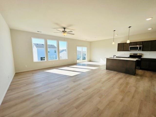 kitchen with an island with sink, appliances with stainless steel finishes, open floor plan, decorative light fixtures, and light countertops