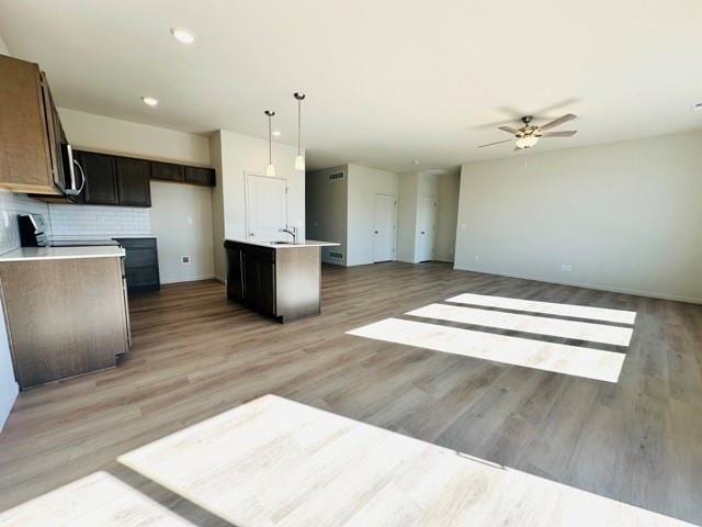 kitchen with decorative light fixtures, a center island with sink, light countertops, stove, and open floor plan