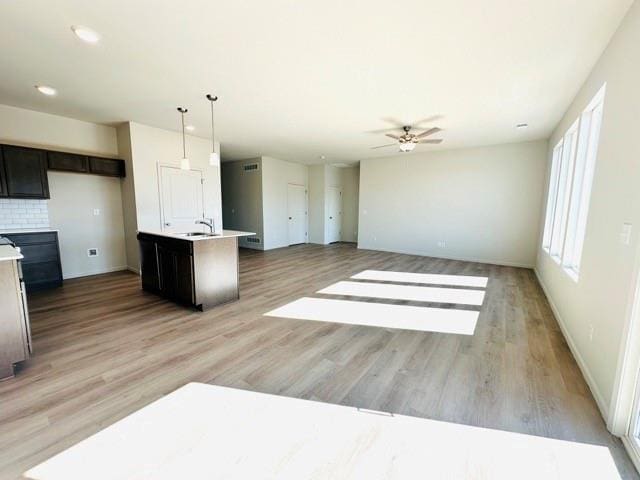 kitchen with light countertops, hanging light fixtures, open floor plan, an island with sink, and light wood-type flooring