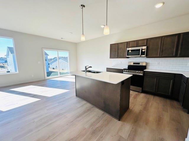 kitchen with a sink, light countertops, appliances with stainless steel finishes, an island with sink, and pendant lighting