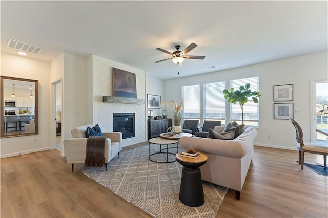 living area featuring a fireplace, a ceiling fan, baseboards, wood finished floors, and visible vents