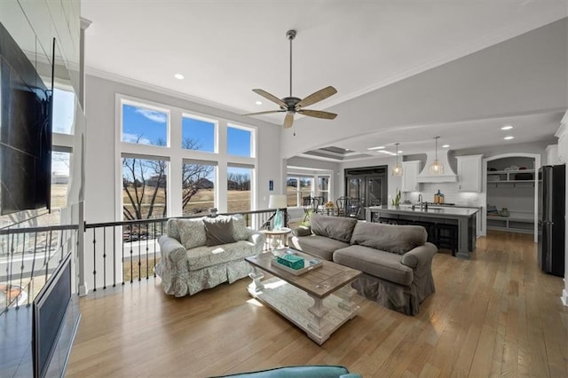 living room with arched walkways, ceiling fan, light wood-style flooring, recessed lighting, and crown molding