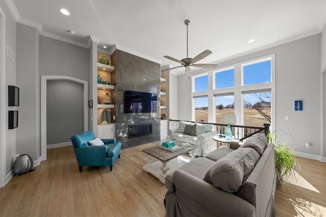 living area with built in shelves, a premium fireplace, light wood-style floors, baseboards, and ornamental molding