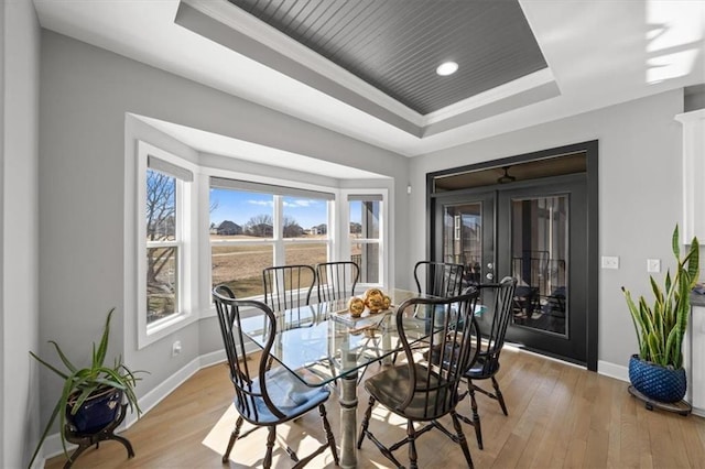 dining room featuring a tray ceiling, light wood-type flooring, and baseboards