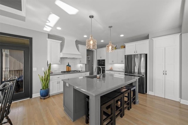 kitchen featuring white cabinets, custom range hood, stainless steel appliances, light wood-type flooring, and a kitchen bar