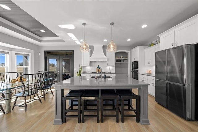 kitchen with premium range hood, a sink, backsplash, freestanding refrigerator, and a raised ceiling