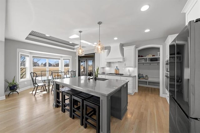 kitchen featuring a tray ceiling, custom exhaust hood, freestanding refrigerator, white cabinetry, and a sink