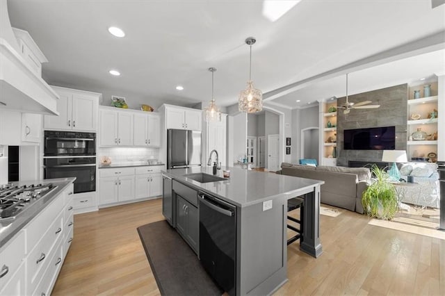 kitchen featuring stainless steel appliances, a breakfast bar, a sink, open floor plan, and light wood finished floors