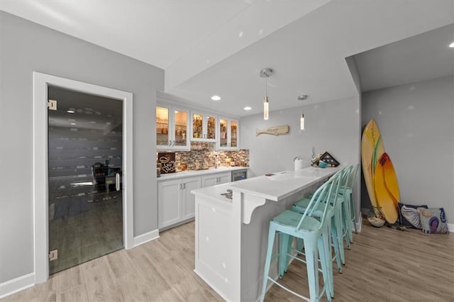 kitchen with a breakfast bar area, light wood finished floors, backsplash, glass insert cabinets, and white cabinetry