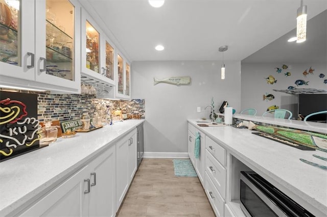 kitchen featuring a sink, white cabinets, hanging light fixtures, decorative backsplash, and glass insert cabinets