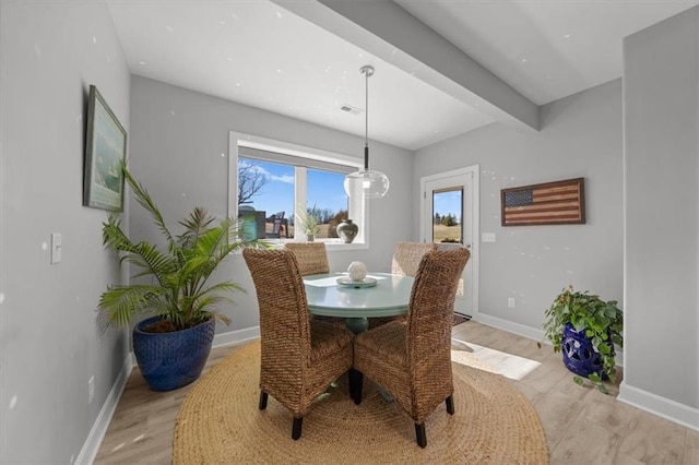 dining space with light wood-type flooring, baseboards, and beam ceiling